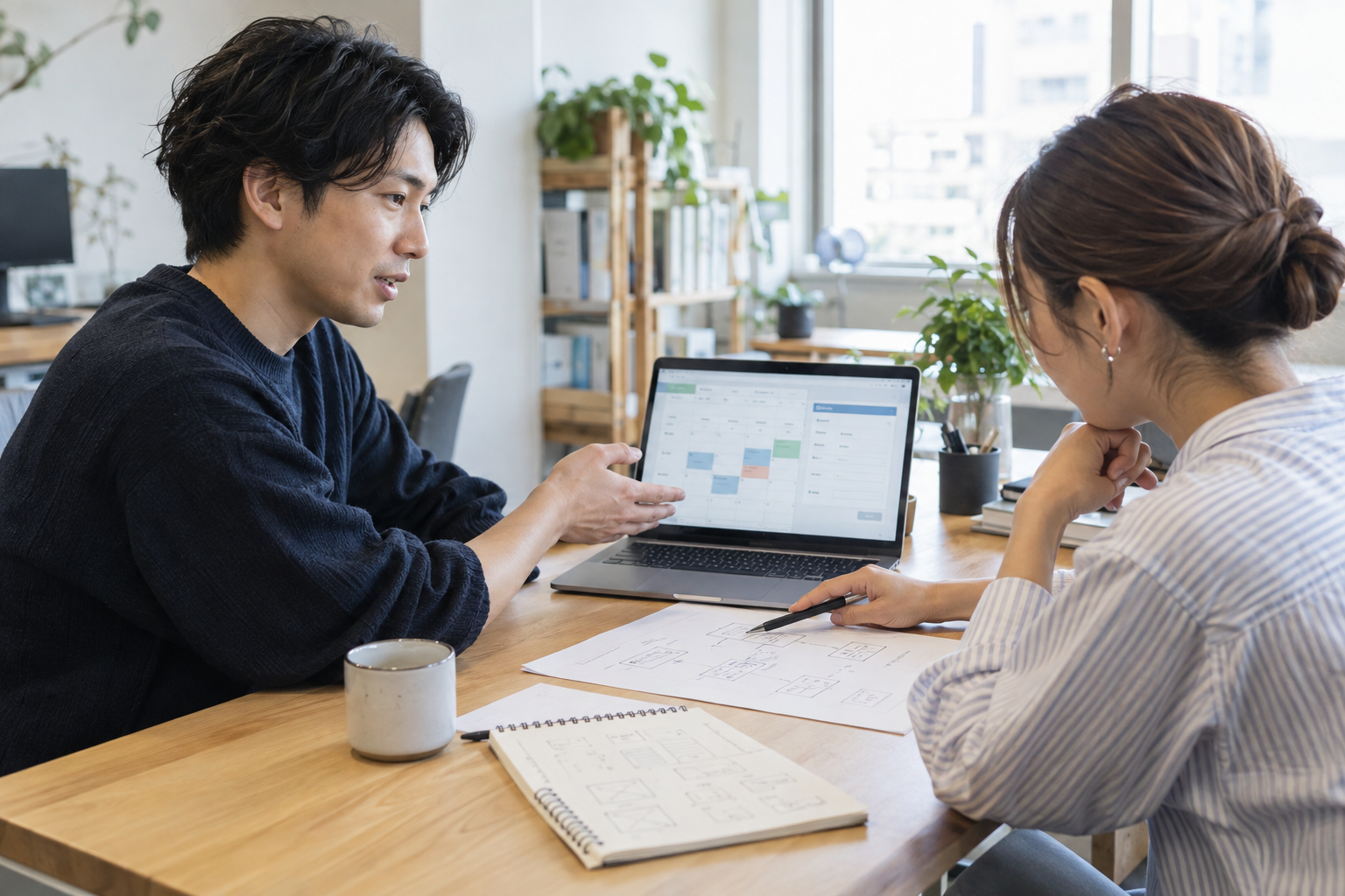 試作したシステムの画面と業務フローの図を見ながら、仕様を相談する二人のイメージ